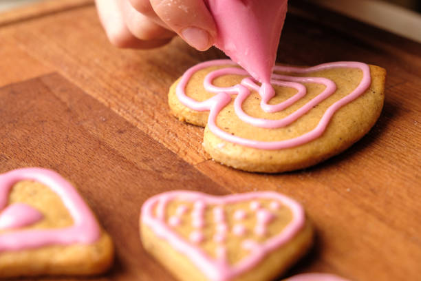 oblodzenie walentynek. kobieta dekorowanie pierniki ciasteczka w kształcie serca na drewnianym stole. - heart shaped cookie zdjęcia i obrazy z banku zdjęć