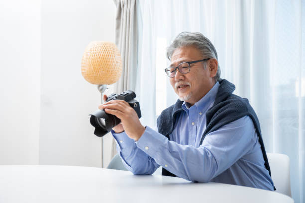 居間でカメラに触れる先輩男性 - シニア世代 写真 ストックフォトと画像