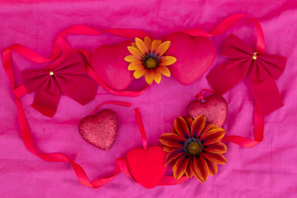 Hearts, bows, ribbon and flowers lie on the red fabric.