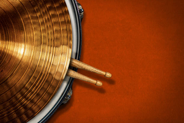 Golden Cymbal on a Snare Drum with two Wooden Drumsticks - Percussion Instrument Closeup of a golden colored cymbal on a snare drum with two wooden drumsticks on an orange velvet background with copy space. Percussion instrument. italian music stock pictures, royalty-free photos & images