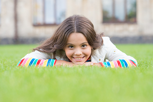 Look at her now. School break for rest. Adorable pupil. Girl kid laying lawn. Girl school uniform enjoy relax. Importance of relaxation. Little schoolgirl. Relax at school yard. Kid relaxing outdoors.