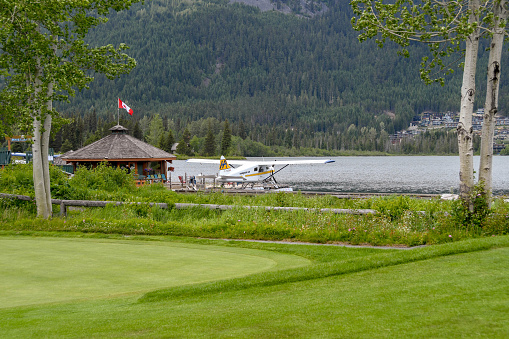 Whistler, British Columbia, Canada - June 2018: Scenic view of the seaplane terminal in Whistler with a Harbour Air seaplane tied up at the jetty. In the foreground is the putting green of a golf course.