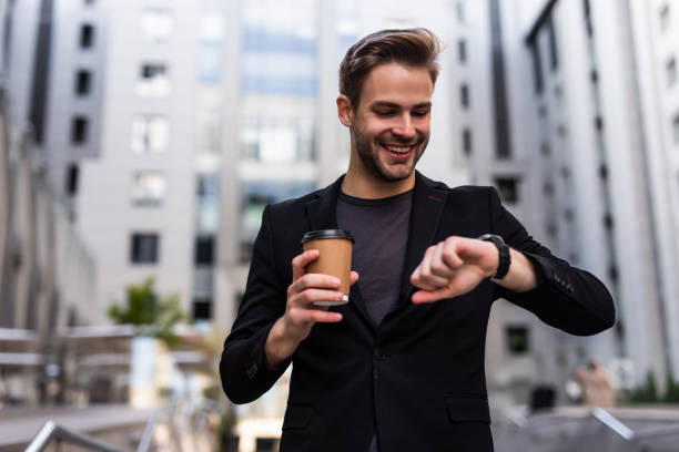 istock Confident male entrepreneur checking time on watch during break while hurrying for meeting. Serious businessman in formal suit standing on urban settings with coffee takeaway looking at wristwatch 1293477332