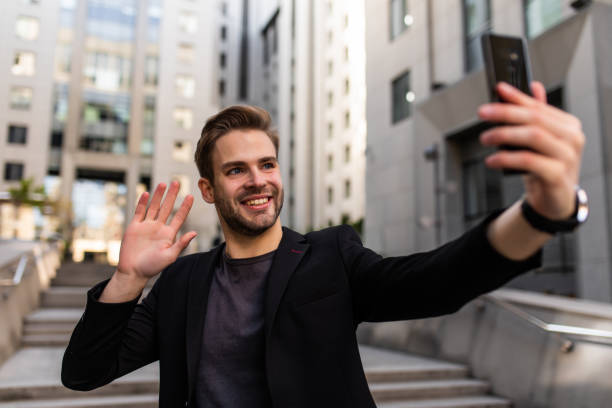 istock Beautiful businessman dressed in formal suit smiling at camera and taking selfie while standing outside 1293479661