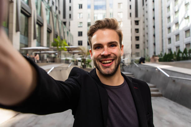 istock Beautiful businessman dressed in formal suit smiling at camera and taking selfie while standing outside 1293482343