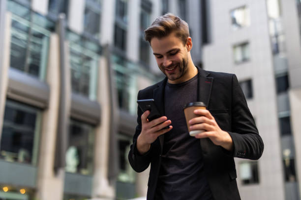 istock Confident young businessman using cell phone and drinking coffee in the city 1293482411