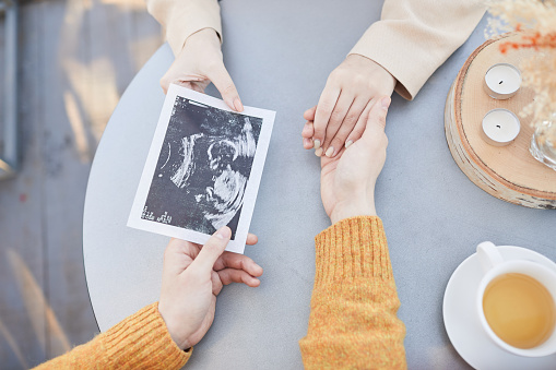 Close-up of couple sitting at the table with tea holding hands and looking at first ultrasound of their baby