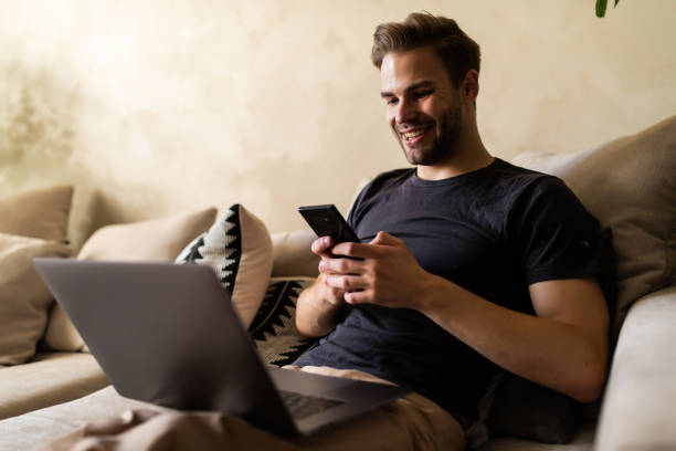 istock Young handsome man using his smartphone for online banking - sitting on sofa with laptop on couch 1293483220