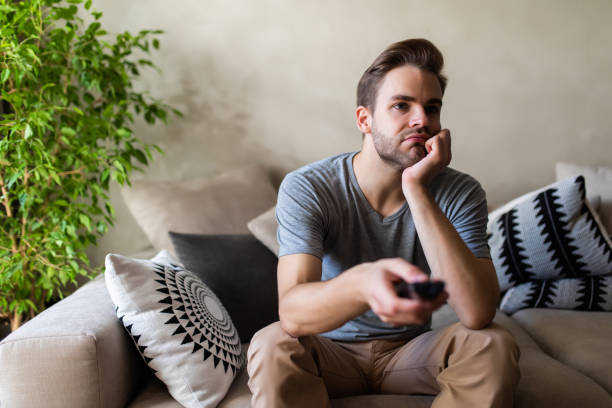 istock Handsome man on cosy sofa getting bored of tv programs, Social distancing and self isolation in quarantine lockdown for Coronavirus Covdi19 1293483309