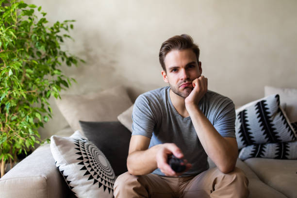 istock Handsome man on cosy sofa getting bored of tv programs, Social distancing and self isolation in quarantine lockdown for Coronavirus Covdi19 1293484490