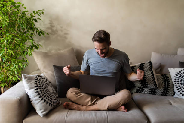 istock Handsome excited young man with laptop at home sitting on a couch 1293484531