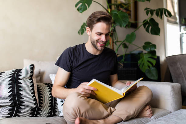 istock Smiling relaxed man reading a book lying on sofa at home 1293484719