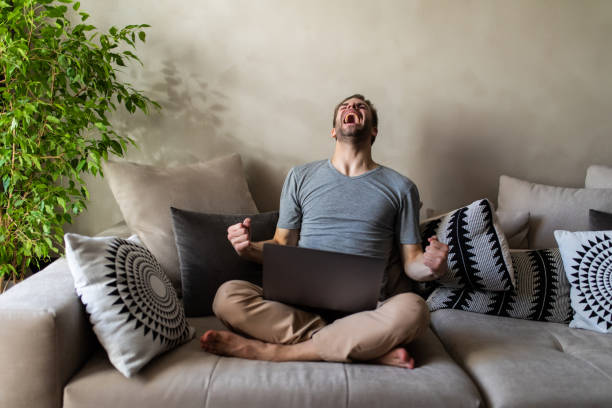 istock Handsome excited young man with laptop at home sitting on a couch 1293484848