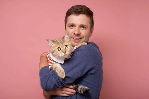 istock A man with an orange tabby cat isolated on pink background. 1293485804