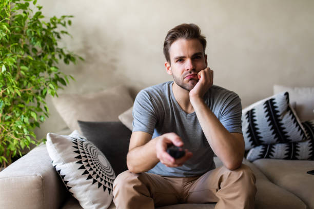 istock Handsome man on cosy sofa getting bored of tv programs, Social distancing and self isolation in quarantine lockdown for Coronavirus Covdi19 1293486438