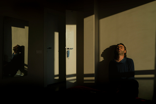Adam eve akan güneş ışığında güneşleniyor. Koruyucu maskesi kapı kolunda asılı olan sıkılmış adam güneş ışığında rahatlatıcı bir şekilde fotoğraflandı.