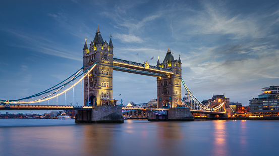 The iconic span of Tower Bridge spotlit at night overlooking the River Thames and The Shard in the heart of London, UK.