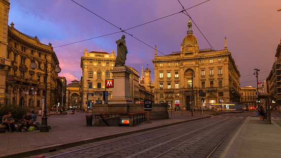 Cordusio Square and Dante street with surrounding palaces, houses and buildings at sunset timelapse in Italian capital of fashion and luxury. Monument to writer and poet Giuseppe Parini. Trams passing by