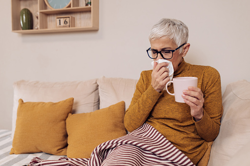Senior woman having a flu, resting in the bed and drinking tea.
