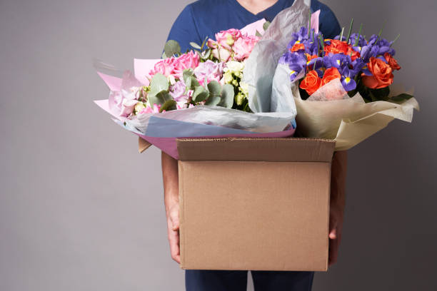 White male courier holding a large cardboard box with several bouquets