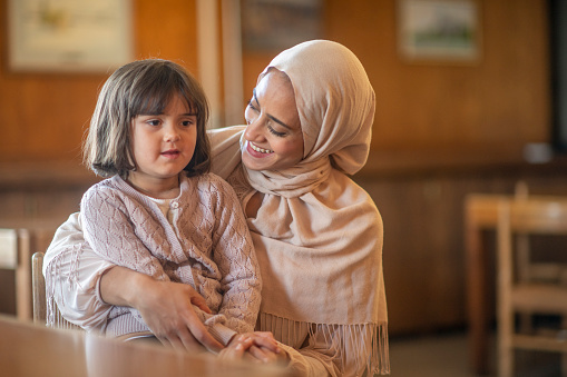 A muslim mother looks at her daughter lovingly as she sits on her lap.