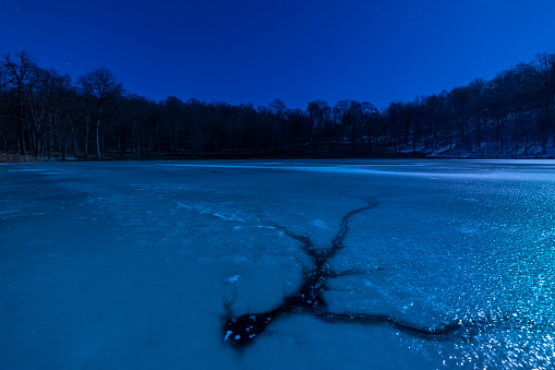 Beautiful winter night landscape. Frozen lake with crack on the ice, beautiful forest. Starry sky