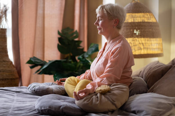 donna caucasica anziana che medita praticando yoga al chiuso. - pranayama foto e immagini stock