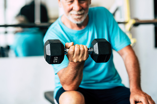 adult man and mature senior at the gym working his body with dumbbell - one man hapy training indoors sitted on the bench