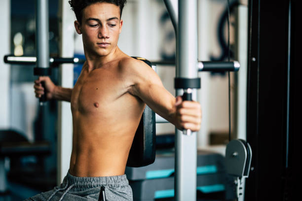 teenager alone at the gym doing exercises and looking his muscles - fitnbess and healthy lifestyle - athelete training his body to be happy