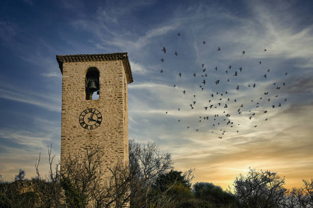 Piegon, France - December 22, 2020. view of an old stone bell tower located on a hill in Provence during a majestic sunset. in the sky, many birds are visible.