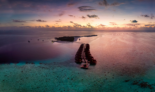 Beautifull aerial view to a tropical island in the Maldives, Indian Ocean, with coral reefs and water bungalows during sunset time