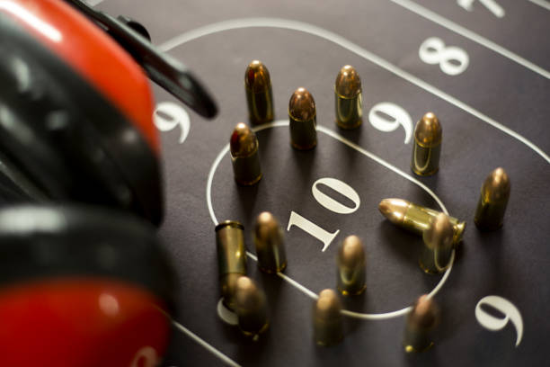 Gun range earmuffs and ammunition on shooting target in display case.