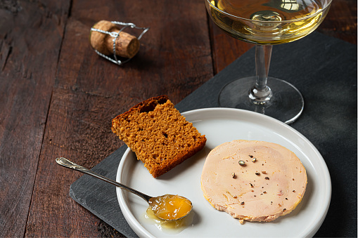 Traditional French foie gras, gingerbread, candied onion in the teaspoon and a glass of champagne on the dark table