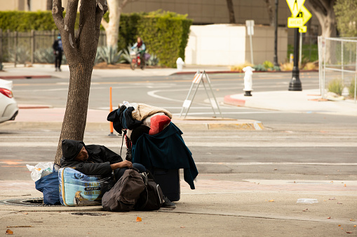 Santa Ana, California, USA - December 20, 2020: A homeless individual sits on a sidewalk in the heart of the civic center in Santa Ana.