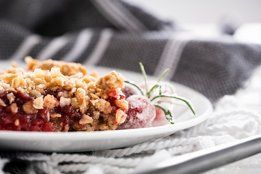 A piece of cranberry crumble on a white plate garnished with sugared cranberries and a sprig of rosemary.