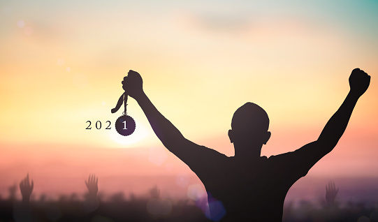 Success new year 2021 concept: Silhouette winner hand holding gold medal reward with text for 2021 against blurred sunset background