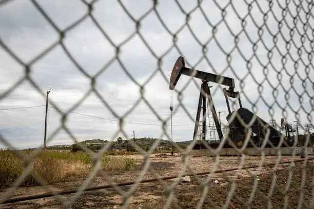 Photo of Oil Pump Rig in Cloudy Rough Weather with Chain Link Fence