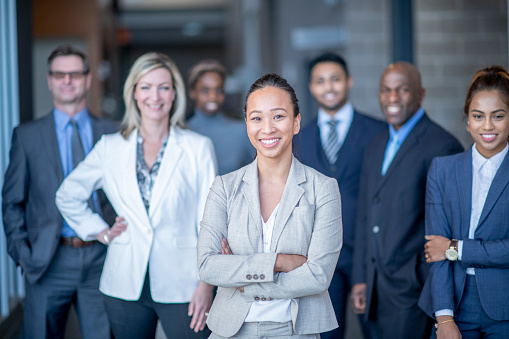 A multi ethnic group of young professionals working together in an office poses together for a photo in their business attire.