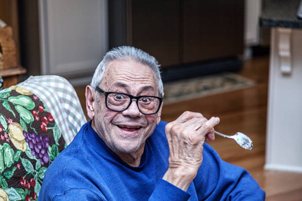 пожилой старший человек делает смешное лицо, держа десертную ложку - raised eyebrows making a face men stubble стоковые фото и изображения