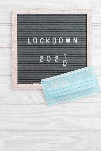 istock Flatlay letter board with message text lockdown 2021 and grey cloth protective face mask. Lock down loading concept. 1293553677