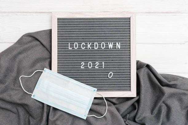 istock Flatlay letter board with message text lockdown 2021 and grey cloth protective face mask. Lock down loading concept. 1293553683