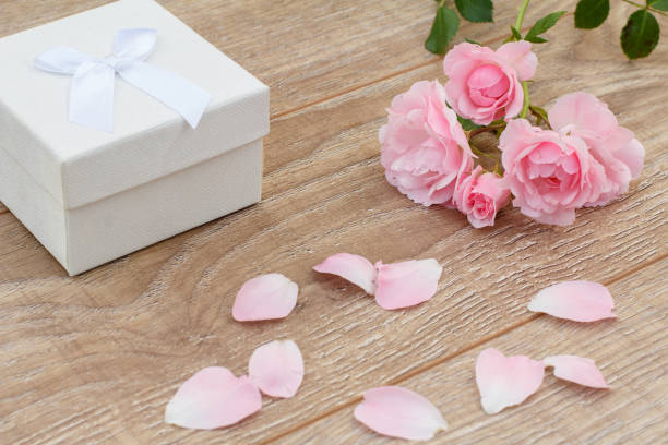 White gift box, rose petals and beautiful pink roses on the wooden background. Concept of giving a gift on holidays. Top view.