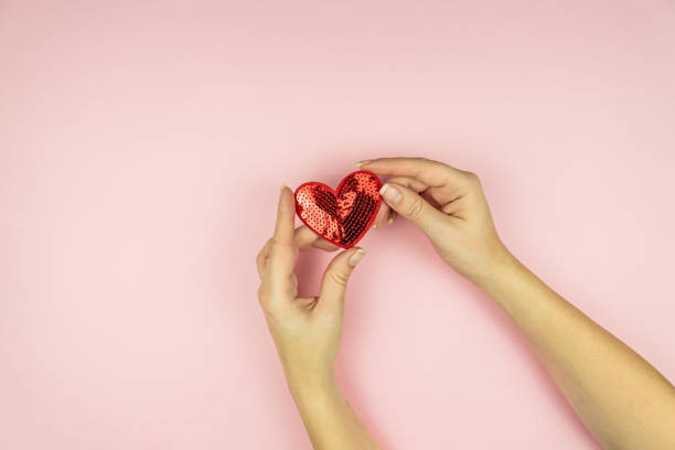 istock Female hands holding red sequin heart on pink background. Creative minimal layout with copy space 1293569547