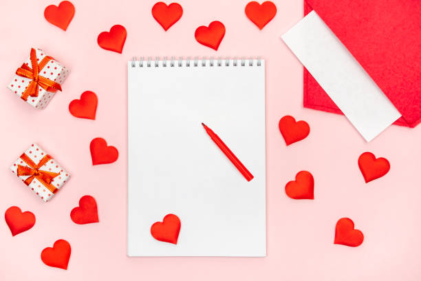 istock Flatlay notepad mock up with felt-tip pen with a red envelope with hearts and gifts on a pink background. Concept of valentine's day and writing love letters 1293570624