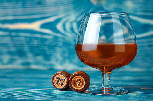 a glass of cognac and wooden barrels with the number seven on a blue wooden background