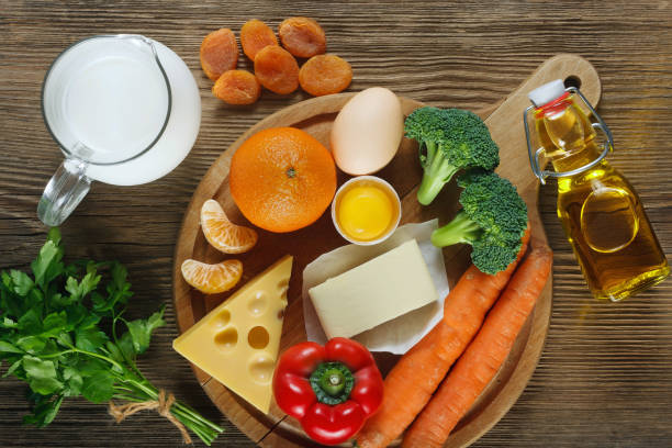 Vitamin A in food. Vitamin A in food. Natural products rich in vitamin A as tangerine, red pepper, parsley leaves, dried apricots, carrots, broccoli, butter, yellow cheese, milk, egg yolk and cod liver oil. Wooden table as background. vitamin a nutrient stock pictures, royalty-free photos & images