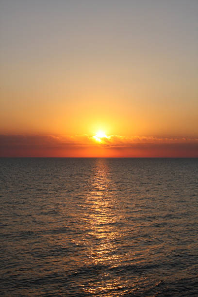 istock Sunset. Sun sets behind sea horizon, turning clouds red and orange. Vertical orientation 1293580635