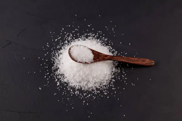 Glutamic acid monosodium salt on dark background. Msg or Food additive E621 in wooden spoon, top view. Selective focus, copy space. The additive is used in food industry.