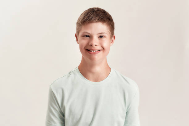 istock Portrait of cheerful disabled boy with Down syndrome smiling at camera while posing isolated over white background 1293588321