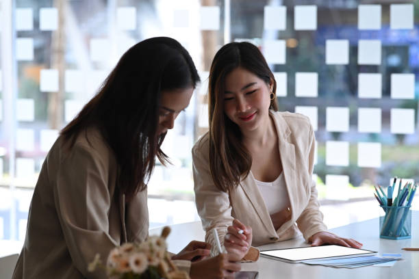 istock Two businesswoman using digital tablet discussing online project together while sitting in office room. 1293592217